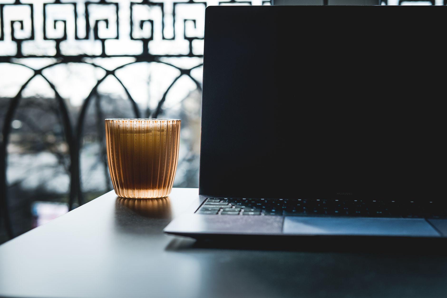 Ordinateur portable sur une table noire avec un verre de boisson, en plein soleil sur un balcon.